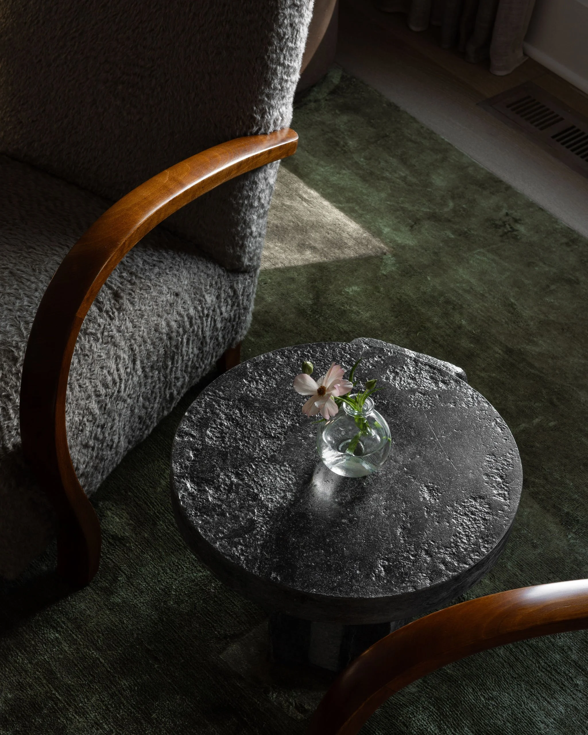 Reupholstered vintage cabinetmaker chairs with a stone side table and a deep green linen rug.