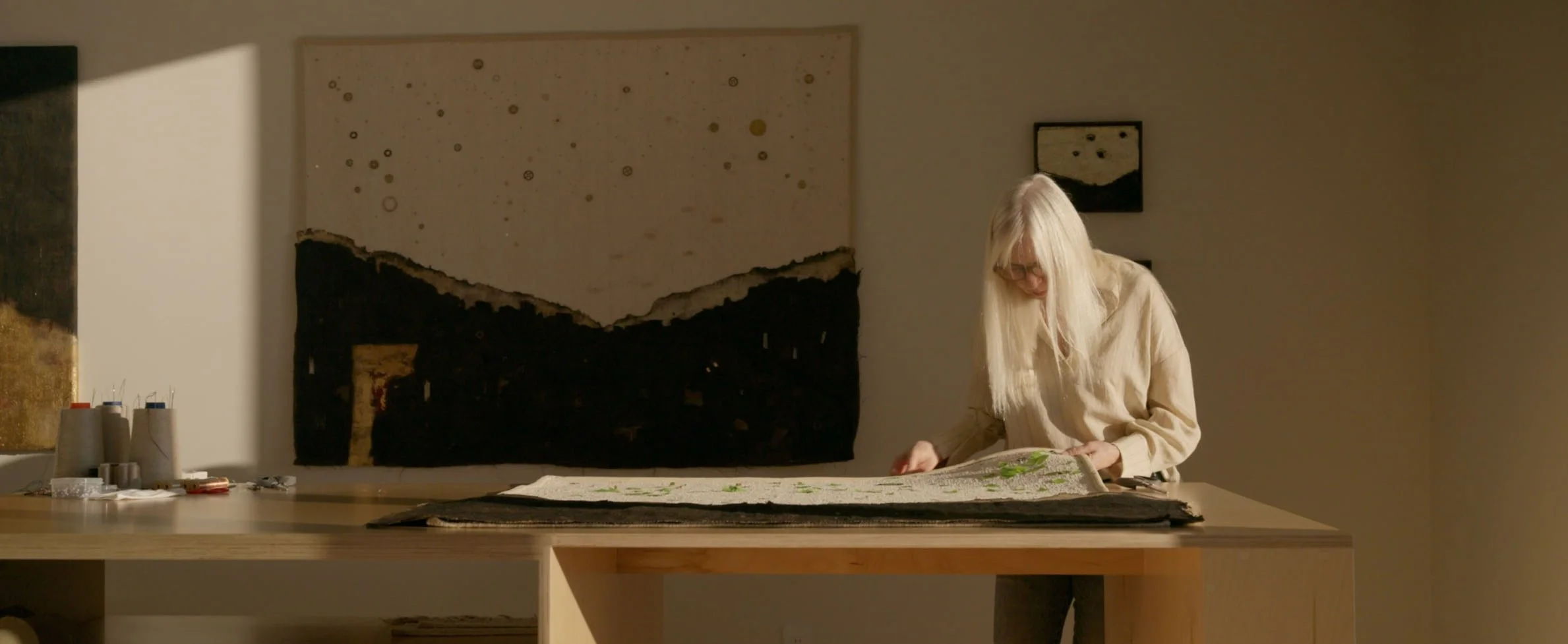 Laura Roberts in her studio, working over a large textile artwork on a wood table.