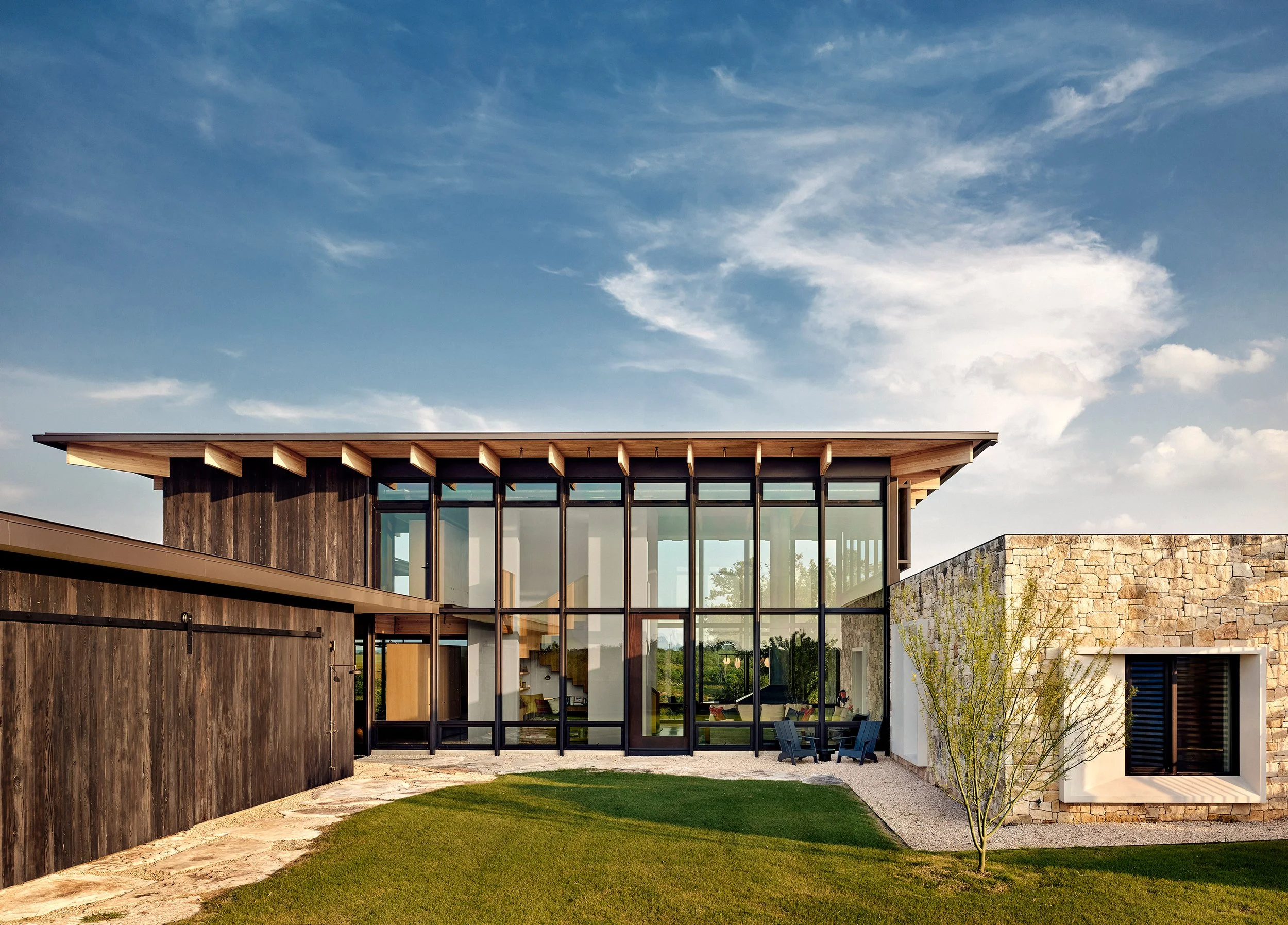 Modern Hill Country home on the Llano River, featuring Texas limestone, expansive glass walls, and shou sugi ban wood siding integrated into the natural landscape.