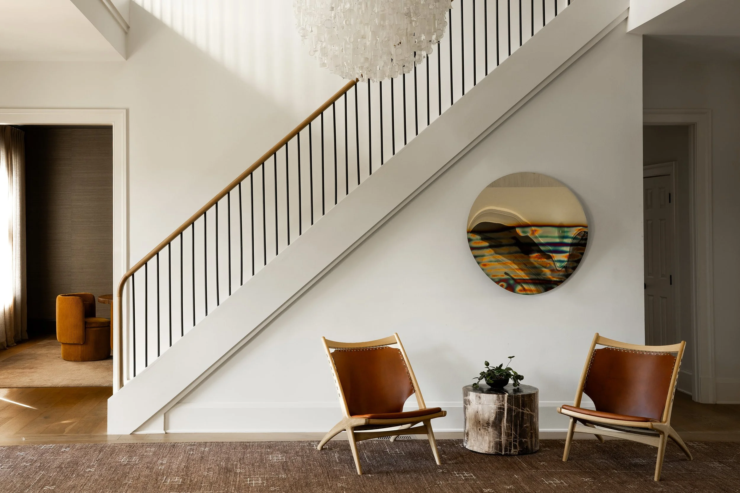 Renovated stair hall in a McLean, VA home featuring a sculptural Tide chandelier by Stuart Haygarth, custom stair railing, artful stainless steel mirror by Anton Hendrik Denys, and a bespoke Battilossi rug.