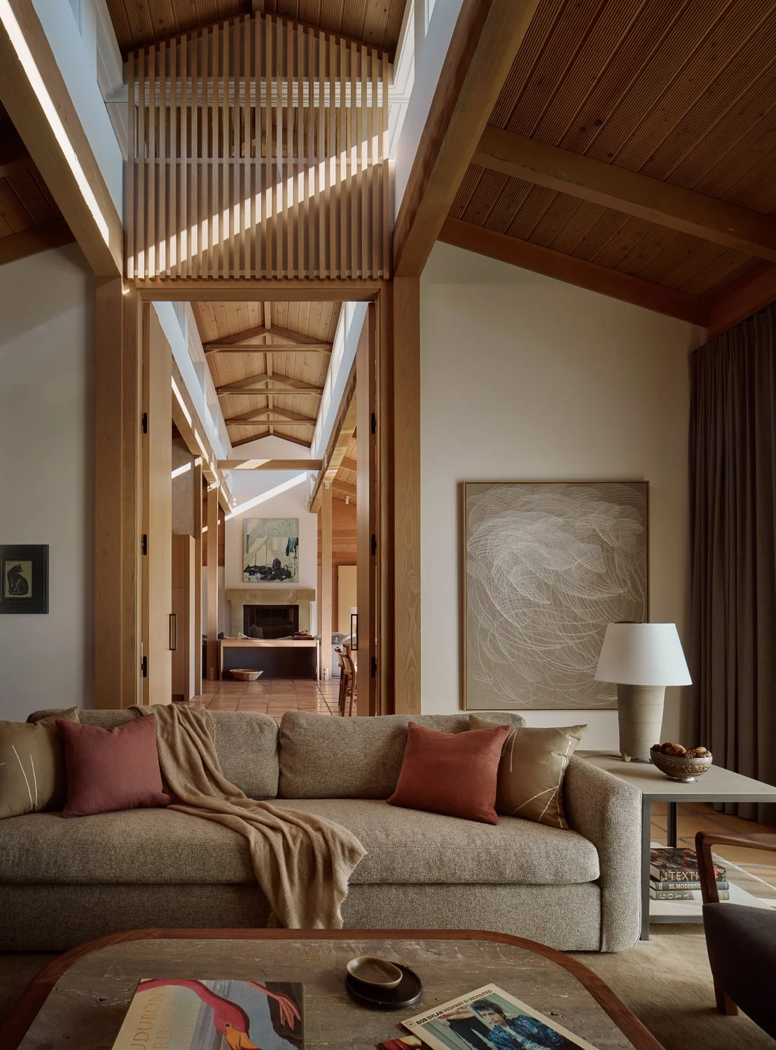Den in a Sonoma, California home, featuring a Verellen sofa, custom coffee table and side table by Petrified Design and a large abstract painting by Athamy Armas, with a view through white oak doors to the living room beyond.
