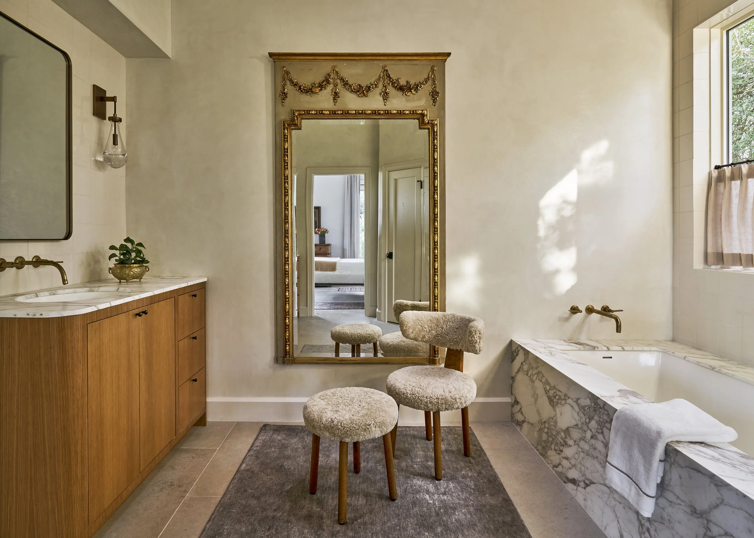 Bathroom with a marble tub enclosure, custom wood vanity, plaster walls, a Van Ghent linen rug, and an antique trumeau mirror.